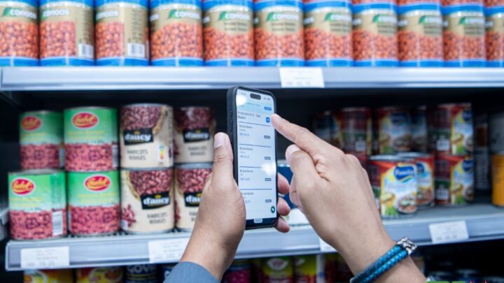 Een smartphone met de prijscontrole-app SRD Check voor een schap met bonen in een supermarkt.