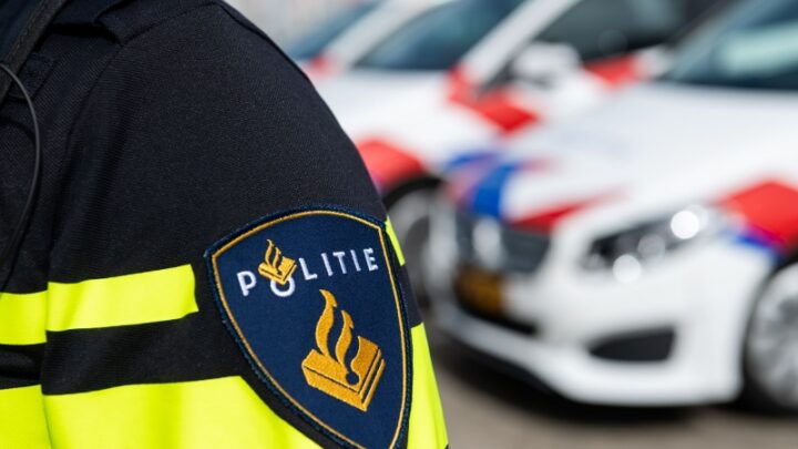 Politie-embleem op een uniform met politieauto’s op de achtergrond.